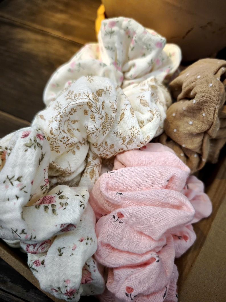 May include: A selection of fabric scrunchies in different colours and patterns. The scrunchies include white with gold floral, white with pink floral, pink with small red flowers, and brown with white polka dots.