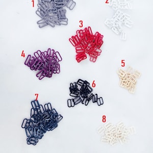 May include: Assortment of eight different colours of metal bra strap sliders. The colours are grey, white, red, purple, beige, black, and cream.