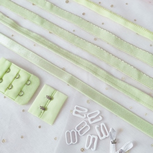 May include: A set of light green bra strap adjusters, hooks, and rings. The set includes two pieces of fabric with hooks and eyes, two pieces of fabric with metal rings, and a set of white plastic rings and hooks.