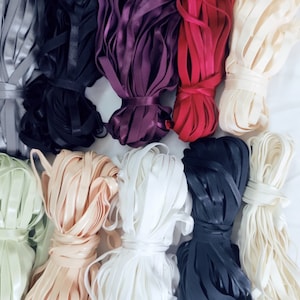 May include: Assortment of 10 spools of different colored elastic ribbon. The colors include gray, black, purple, red, beige, light green, peach, white, dark blue, and cream.