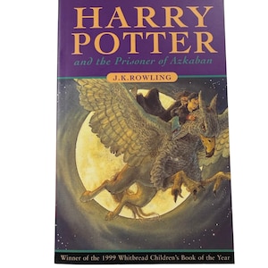 May include: A paperback book titled Harry Potter and the Prisoner of Azkaban by J.K. Rowling. The cover features a purple top section with yellow text and an illustration of a person riding a large, winged creature in front of a full moon.