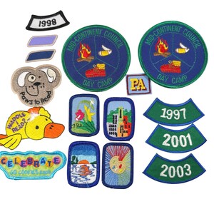 May include: A collection of embroidered fabric patches featuring various designs including two circular Mid-Continent Council Day Camp patches, a Paws to Read dog face, a Waddle I Read duck, a Celebrate GS Cookies 2008 patch, and several rectangular and curved year patches.