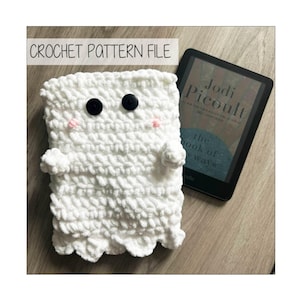 Pode incluir: Uma capa de Kindle branca de crochê em forma de fantasma, com olhos de botão pretos e bochechas rosadas. A capa tem braços pequenos e uma borda inferior ondulada. O texto "CROCHET PATTERN FILE" está no topo. Um leitor Kindle é visível ao fundo.