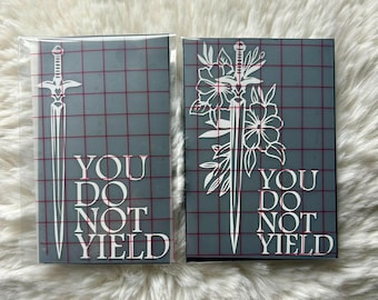 May include: Two rectangular vinyl decals on a grid backing. The left decal features a white sword and the text "YOU DO NOT YIELD". The right decal features a white sword intertwined with floral elements and the same text "YOU DO NOT YIELD".
