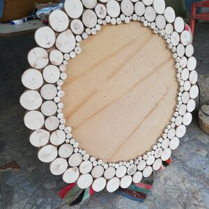 May include: A large, round wooden mirror with a natural wood slice border. The mirror's frame is made of numerous small, light-colored wood rounds, creating a rustic and textured design. The mirror's center is a light brown, unfinished wood.