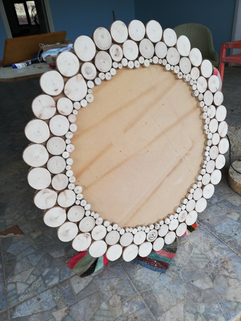 May include: A large, round wooden mirror with a natural wood slice border. The mirror's frame is made of numerous small, light-colored wood rounds, creating a rustic and textured design. The mirror's center is a light brown, unfinished wood.