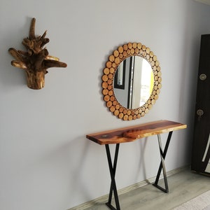 May include: A wooden console table with a live edge top and black metal legs. A round mirror with a wooden log slice frame hangs above the table. A decorative wooden wall art piece is to the left.