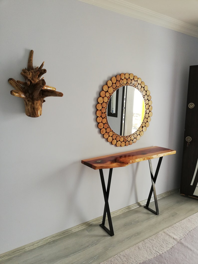 May include: A wooden console table with a live edge top and black metal legs. A round mirror with a wooden log slice frame hangs above the table. A decorative wooden wall art piece is to the left.