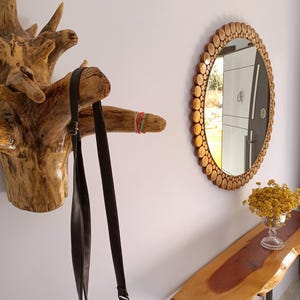 May include: A rustic entryway scene featuring a wooden coat rack, a round mirror with a wooden frame, and a live-edge console table. A dark brown shoulder bag hangs from the coat rack. A vase of yellow flowers sits on the table.