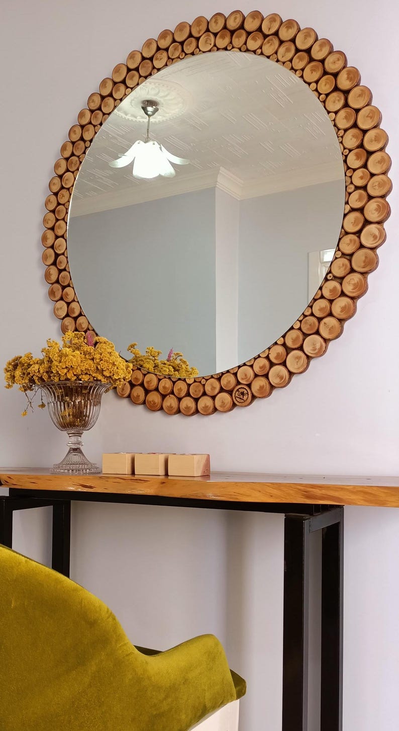 May include: A round mirror with a wooden frame made of small, circular wood pieces. The mirror is mounted on a wall above a wooden console table. A glass vase with yellow flowers and three small wooden boxes are on the table.