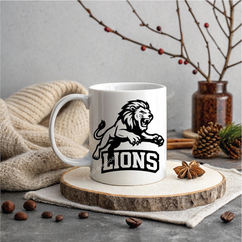 May include: White ceramic mug with a black and white lion illustration and the word "LIONS". The mug is presented on a wooden slice, with a neutral backdrop and decorative items, including a vase and pine cones.