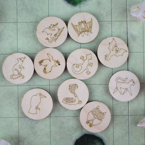 May include: Wooden game tokens featuring engraved animal and fantasy creature designs, such as a dragon, bat, and snake. Dice with gold numbers are scattered around the tokens on a green grid background. A fun game for all ages.