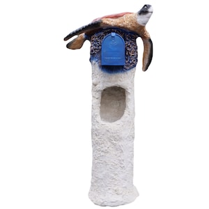 May include: A white concrete mailbox with a blue mailbox door and a sea turtle sculpture on top. The turtle is brown, orange, and tan with a blue and white background.