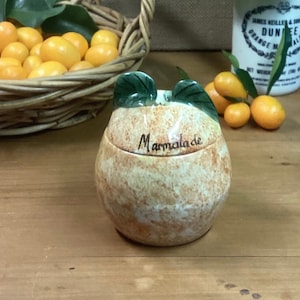 May include: A ceramic marmalade jar shaped like an orange with green leaves on top. The jar has the word "Marmalade" written on it.