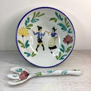 May include: White ceramic bowl with a blue rim, depicting two dancing figures in traditional dress, encircled by floral and leaf motifs. A matching salad fork with a floral design is also visible.