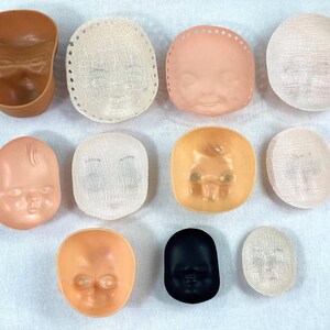 May include: Assortment of ten doll head molds, including a brown plastic mold, a black plastic mold, and eight white plastic molds. Some of the molds have a mesh texture.