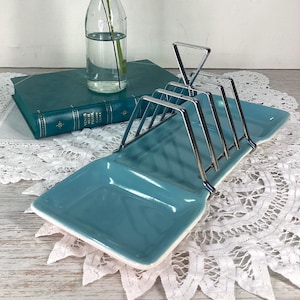 May include: A rectangular teal ceramic toast rack featuring a glossy finish and a chrome metal wire divider structure with four slots. The base is elongated with a smooth, solid surface, and the metal frame is attached to the centre of the tray.