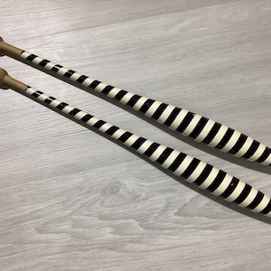 May include: Two juggling clubs featuring a tapered body with a black and white striped pattern. Each club has a smooth, rounded wooden handle at the top end, transitioning into the striped section that widens towards the base of the club.