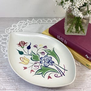 May include: White ceramic serving dish with a leaf shape and a floral design in shades of red, yellow, blue, green, and purple.