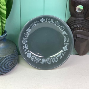 May include: A light blue glass plate with a white design of various fruits and vegetables around the rim.