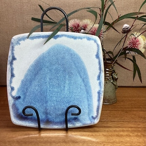 May include: A blue and white ceramic square plate with a raised, rounded design in the centre. The plate is on a black metal stand.