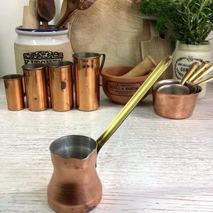 May include: A distressed white wooden sign displaying the word "Welcome" in a handwritten font. A small heart decoration is affixed below the text. The background is a blurred image of a wooden surface, suggesting a rustic aesthetic.