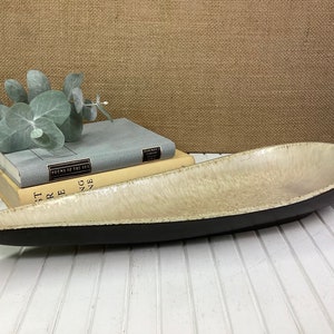 May include: A long, oval-shaped serving dish with a black rim and a white, speckled interior. The dish is made of ceramic and has a rustic, handmade look.