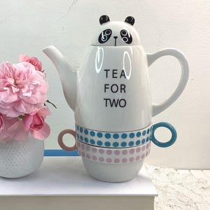 May include: White ceramic teapot with a panda head lid and the text "Tea for Two". The teapot has a matching set of two teacups with blue and pink polka dot designs.
