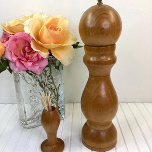 May include: A set of two wooden kitchen utensils. A brown wooden salt and pepper grinder with a brass top and a brown wooden toothpick holder.