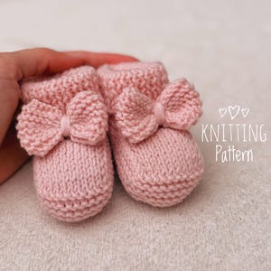 May include: A pair of pink knitted baby booties with bow detailing. The booties are crafted from soft yarn and have a ribbed cuff and a decorative bow on the front. The text "KNITTING Pattern" is visible.