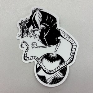 May include: Black and white sticker featuring a rat wearing a gas mask, perched atop a star-shaped design within a circle. The rat's tail curves around the star. The sticker has a white border.