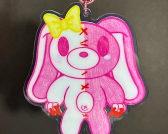 May include: Pink and white plush toy with a yellow bow, stitched seams, and red claws. The toy has a sad expression with tear-shaped eyes.