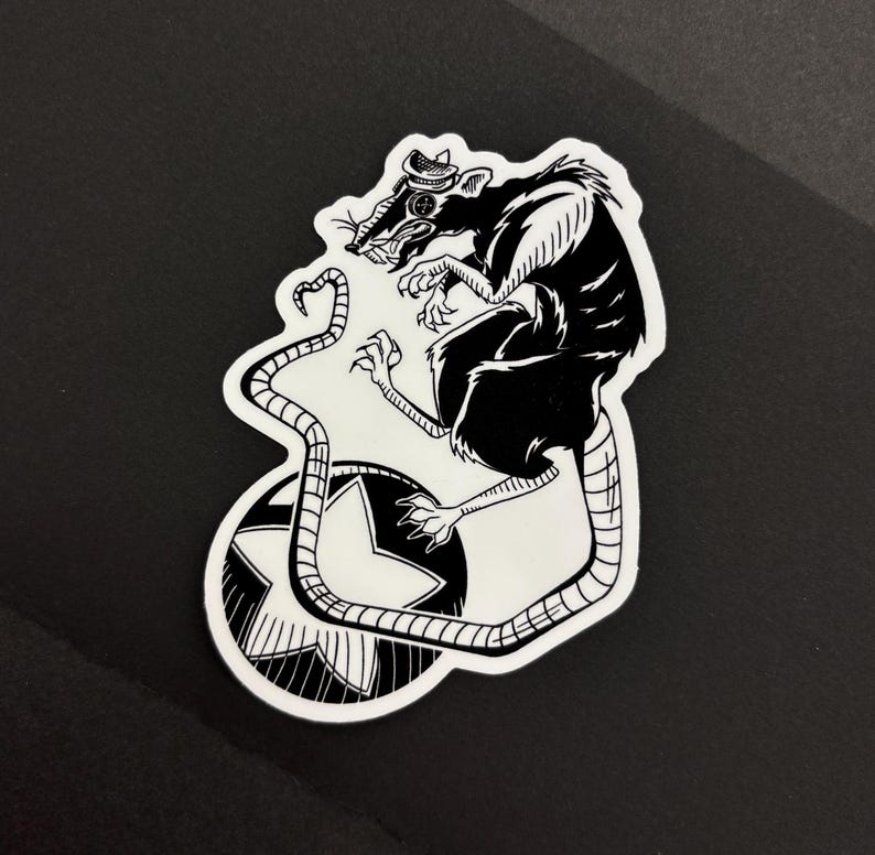 May include: Black and white sticker featuring a rat wearing a hat, perched atop a star-shaped design. The rat has a long tail and is rendered in a detailed, illustrative style. The sticker is die-cut with a white border.