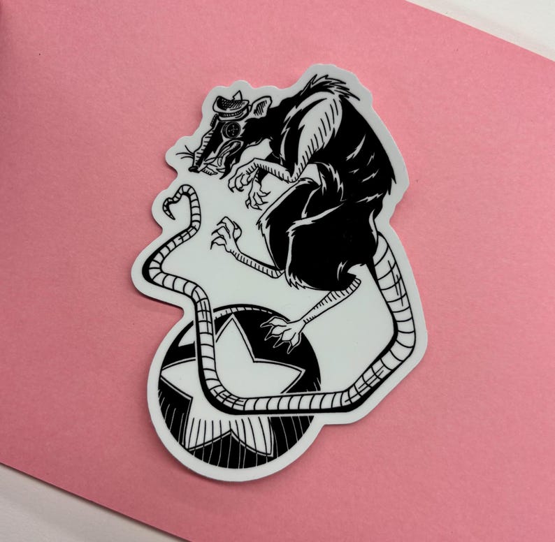 May include: Black and white sticker featuring a rat wearing a hat, with a star design. The rat is perched atop a star-shaped design. The sticker is on a pink background.