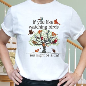 Puede incluir: Camiseta blanca con un gr&aacute;fico de un &aacute;rbol con muchos p&aacute;jaros coloridos y el texto "Si te gusta observar p&aacute;jaros, puede que seas un gato."