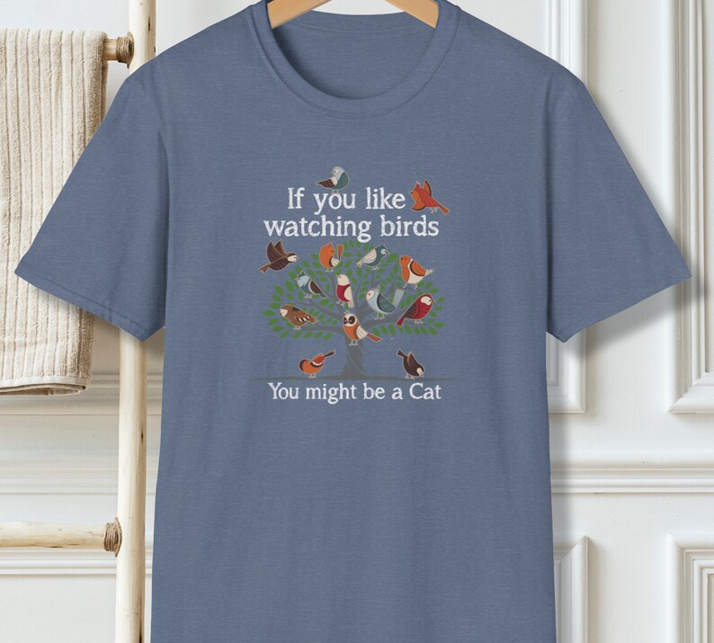 Puede incluir: Una camiseta azul con un gr&aacute;fico blanco de un &aacute;rbol con p&aacute;jaros y el texto "Si te gusta observar p&aacute;jaros Puede que seas un gato".
