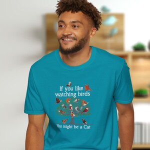 Puede incluir: Una camiseta azul turquesa con un gr&aacute;fico blanco de un &aacute;rbol con p&aacute;jaros en &eacute;l. El texto en la camiseta dice "Si te gusta observar p&aacute;jaros, podr&iacute;as ser un gato."