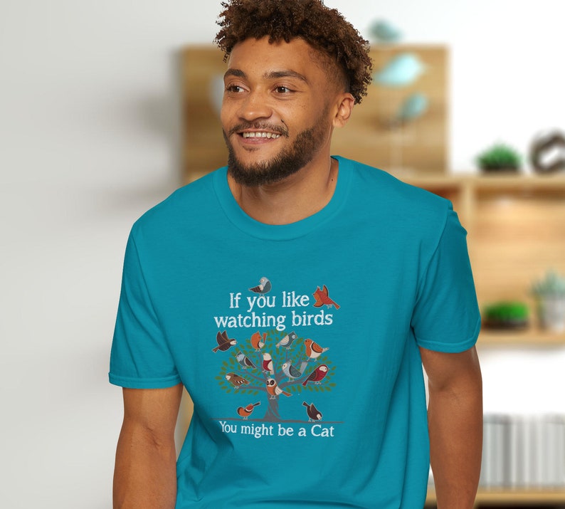 Puede incluir: Una camiseta azul turquesa con un gr&aacute;fico blanco de un &aacute;rbol con p&aacute;jaros en &eacute;l. El texto en la camiseta dice "Si te gusta observar p&aacute;jaros, podr&iacute;as ser un gato."