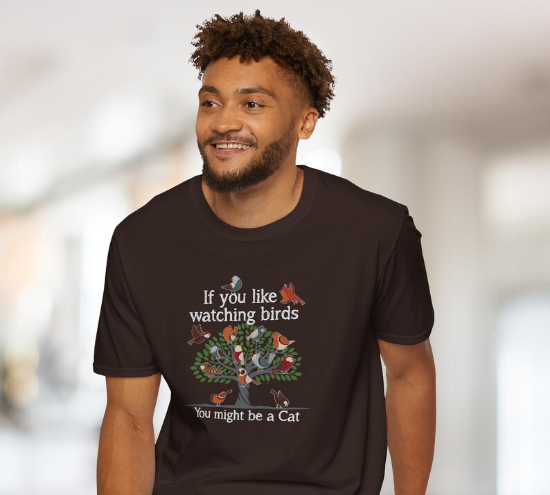 Puede incluir: Una camiseta marr&oacute;n con un gr&aacute;fico de un &aacute;rbol con p&aacute;jaros y el texto "Si te gusta observar p&aacute;jaros Puede que seas un gato."