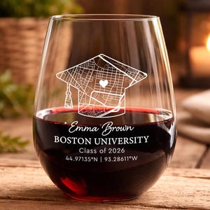 May include: A stemless wine glass filled with red wine. The glass is etched with a graduation cap design and the text "Emma Brown, Boston University, Class of 2026". Coordinates are also included.