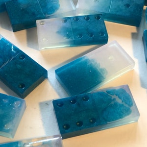 May include: A set of blue and clear resin dominoes with white dots. The dominoes have a marbled effect and are translucent.