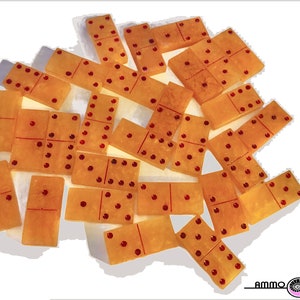 May include: A set of 18 dominoes with a translucent amber color and red dots. The dominoes are scattered on a white surface.