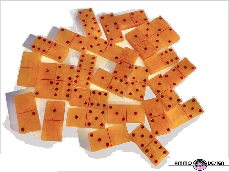 May include: A set of 18 dominoes with a translucent amber color and red dots. The dominoes are scattered on a white surface.