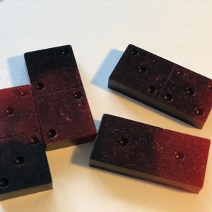 May include: Four dominoes with black and red speckled surfaces. The dominoes have a total of 12 dots.