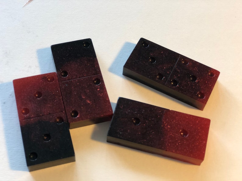 May include: Four dominoes with black and red speckled surfaces. The dominoes have a total of 12 dots.