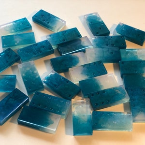 May include: A set of 21 blue and white resin dominoes with a marbled effect. The dominoes are translucent and have a glossy finish.