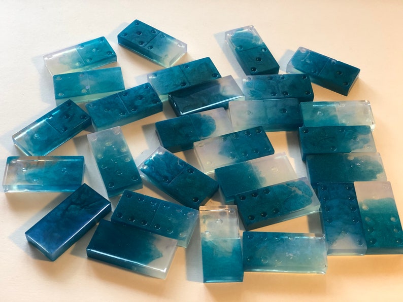 May include: A set of 21 blue and white resin dominoes with a marbled effect. The dominoes are translucent and have a glossy finish.