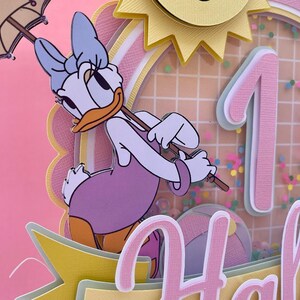 K&ouml;nnte beinhalten: Eine mehrschichtige Papierarbeit in Rosa und Gelb mit einer Comic-Ente, die einen lila Badeanzug tr&auml;gt und einen Regenschirm h&auml;lt. Die Ente steht vor einer pinkfarbenen Zahl Eins mit einer gelben Sonne und einem Gittermuster im Hintergrund. Der Text "Happy" ist am unteren Rand des Bildes sichtbar.