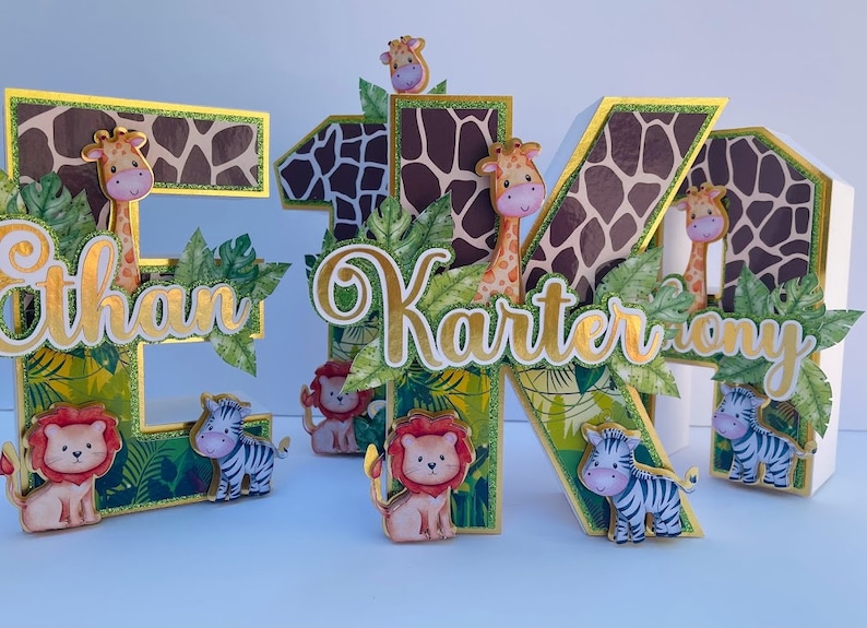 K&ouml;nnte beinhalten: Drei Holzbuchstaben, E, K und O, im Dschungel-Design. Die Buchstaben sind mit gr&uuml;nen Bl&auml;ttern, einer Giraffe, einem Zebra und einem L&ouml;wen verziert. Die Buchstaben ergeben den Namen "Ethan Karter Tony".