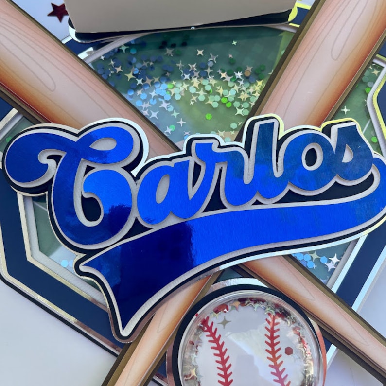 Pu&ograve; includere: Uno striscione con il nome a tema baseball blu e bianco con il nome "Carlos" in un carattere in grassetto e corsivo. Lo striscione &egrave; decorato con mazze da baseball incrociate e una palla da baseball.